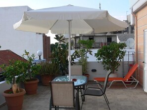 An outdoor patio with a table and chairs, a large umbrella, potted plants, and a red lounge chair.