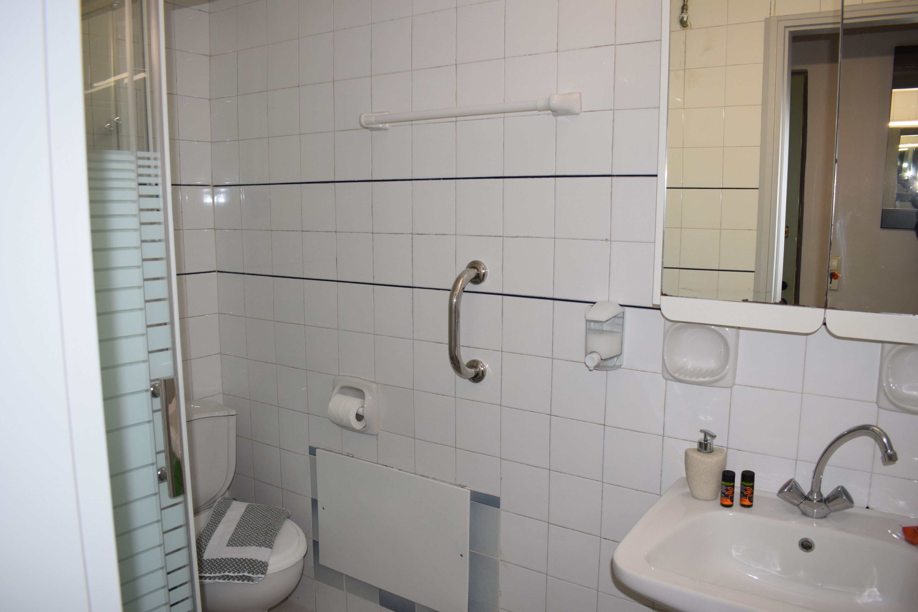Ein Badezimmer mit einem weißen Waschbecken, einem Spiegel, einem Handtuchhalter und einer Toilette.