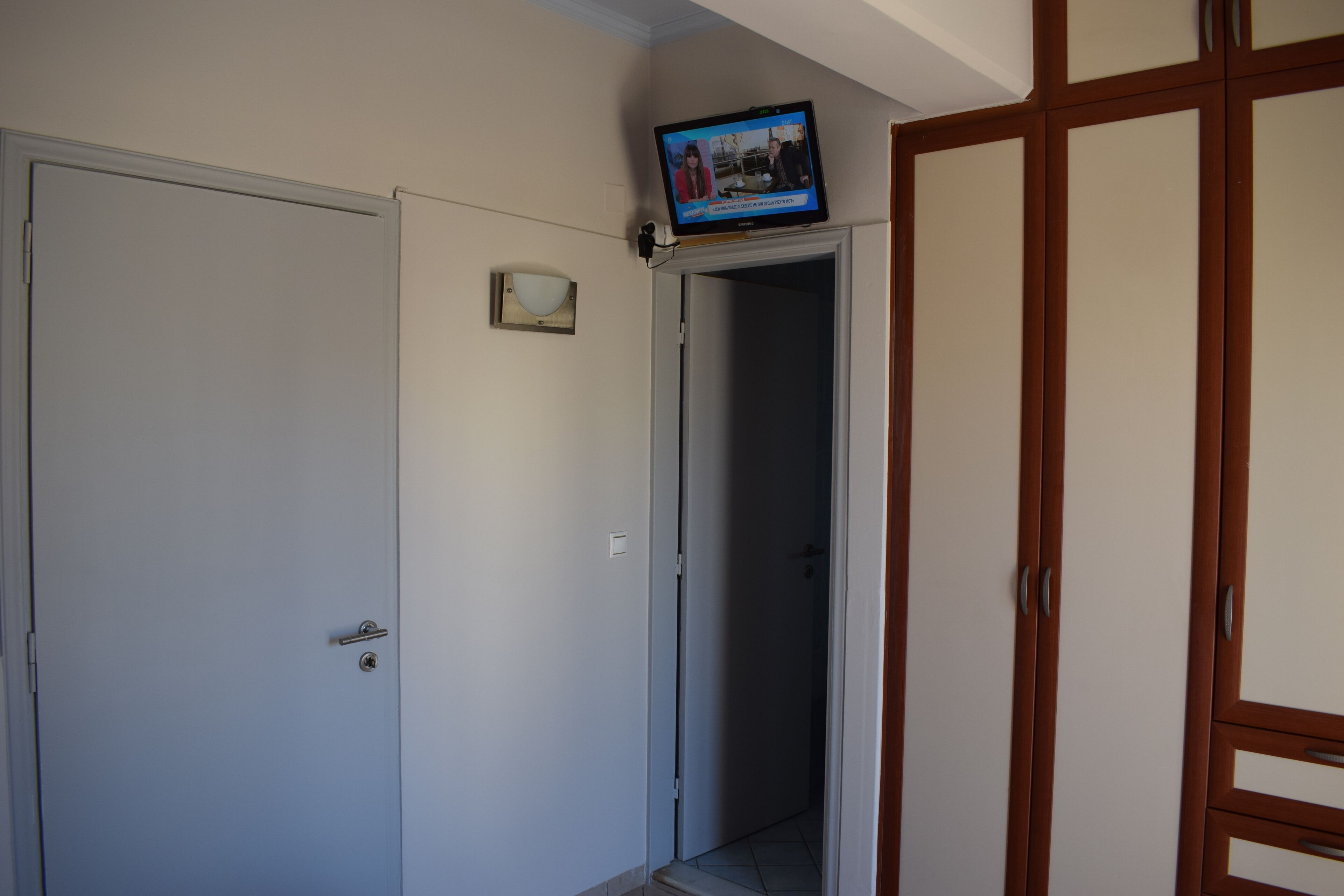 A hallway with a closed door, a television mounted on the wall, and a wooden wardrobe.