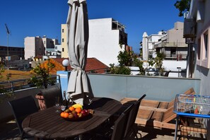 Una terraza en la azotea con una mesa de madera, sillas, un frutero y un carrito de metal.