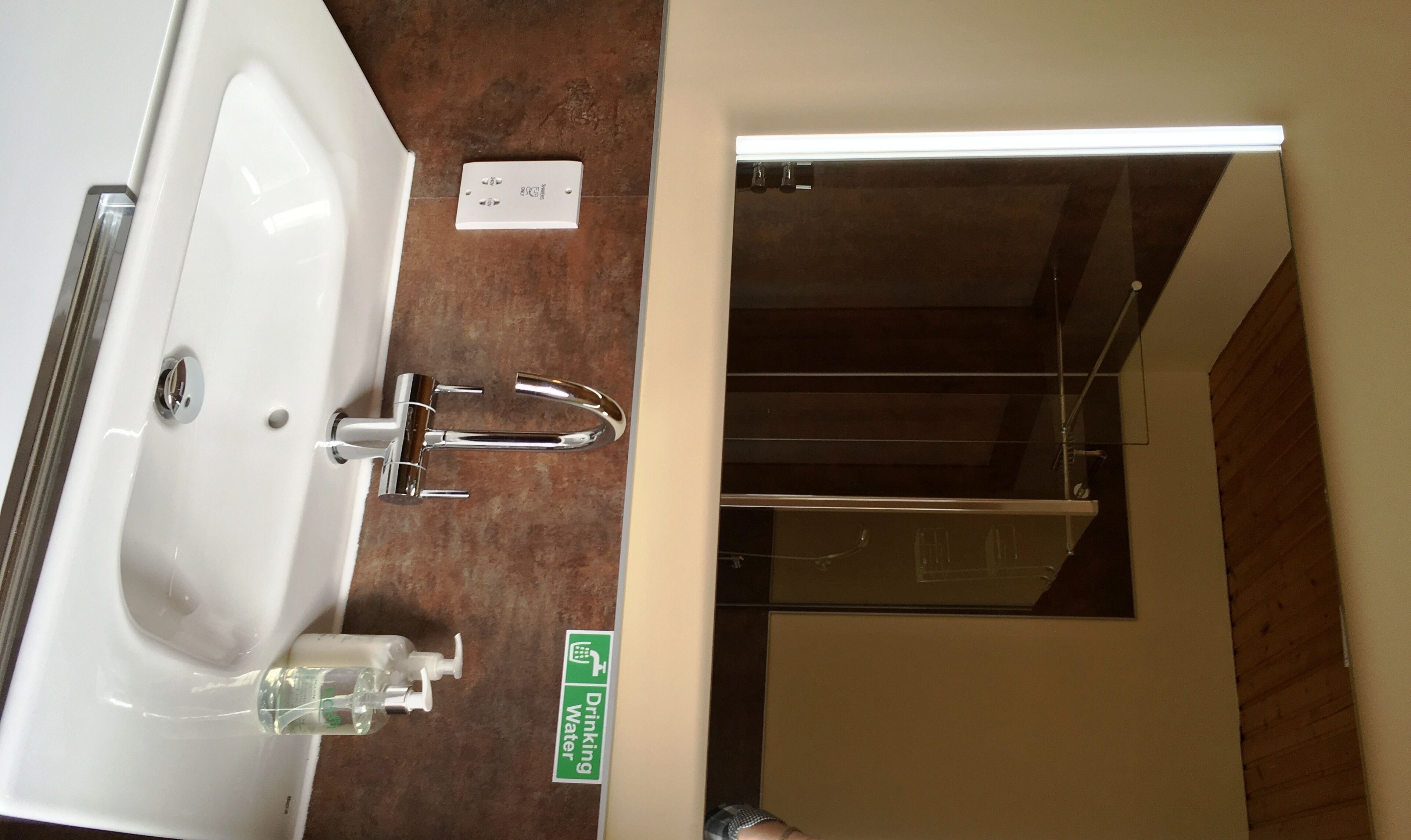 Ein Badezimmer mit Waschbecken, einer Handseifen-Spender und einem Schild, das eine Trinkwasseranlage kennzeichnet.
