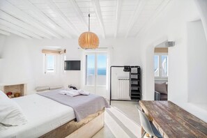Een moderne hotelkamer met een bed, een houten bureau, een televisie en uitzicht op zee.