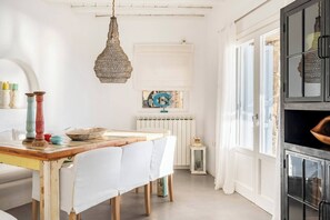 Een keuken met een rustieke houten tafel, witte stoelen, een hanglamp en een raam met uitzicht.