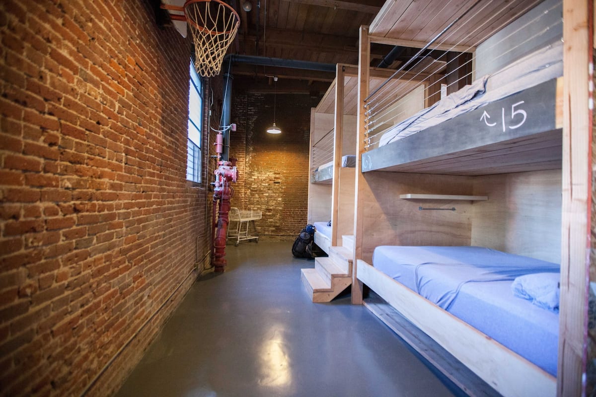 A narrow corridor with brick walls, a basketball hoop, bunk beds, and a staircase.
