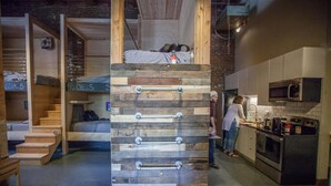 Ein modernes Interieur mit einer Holzleiterkonstruktion, einer Küchenzeile mit Geräten und einer Treppe, die zu einem Schlafzimmer auf dem Dachboden führt.
