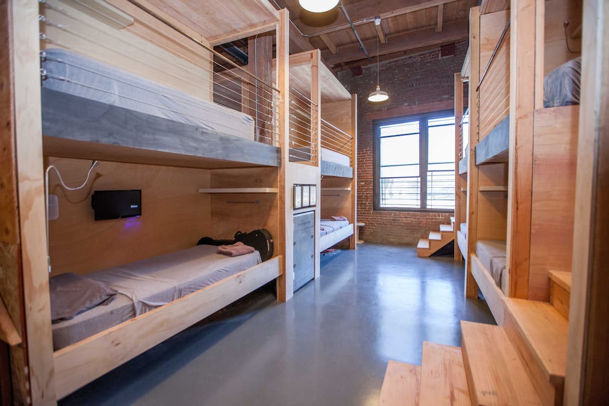 A dormitory-style room with bunk beds, a flat-screen TV, and a brick wall.