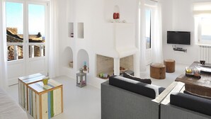 A spacious living room with a large gray sofa, a wooden coffee table, and a television mounted on the wall. - Villa Adella by Mermaid Luxury Villas (Mykonos)