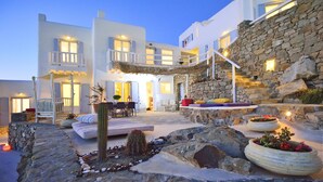 A modern building with a stone facade, outdoor seating area, and potted plants. - Villa Adella by Mermaid Luxury Villas (Mykonos)