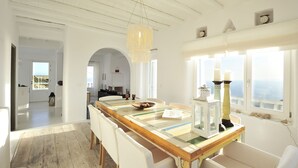 A spacious dining area with a long wooden table, white chairs, and a chandelier. - Villa Adella by Mermaid Luxury Villas (Mykonos)