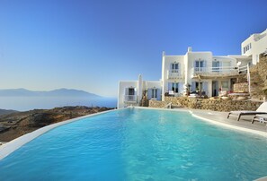 A white building with a pool and a view of the sea.