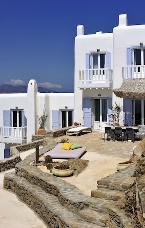 A white building with blue shutters, a stone staircase, and a dining area with outdoor seating.