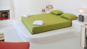 A modern, minimalist bedroom with a green bed, white walls, and a red chair. - Villa Adella by Mermaid Luxury Villas (Mykonos)