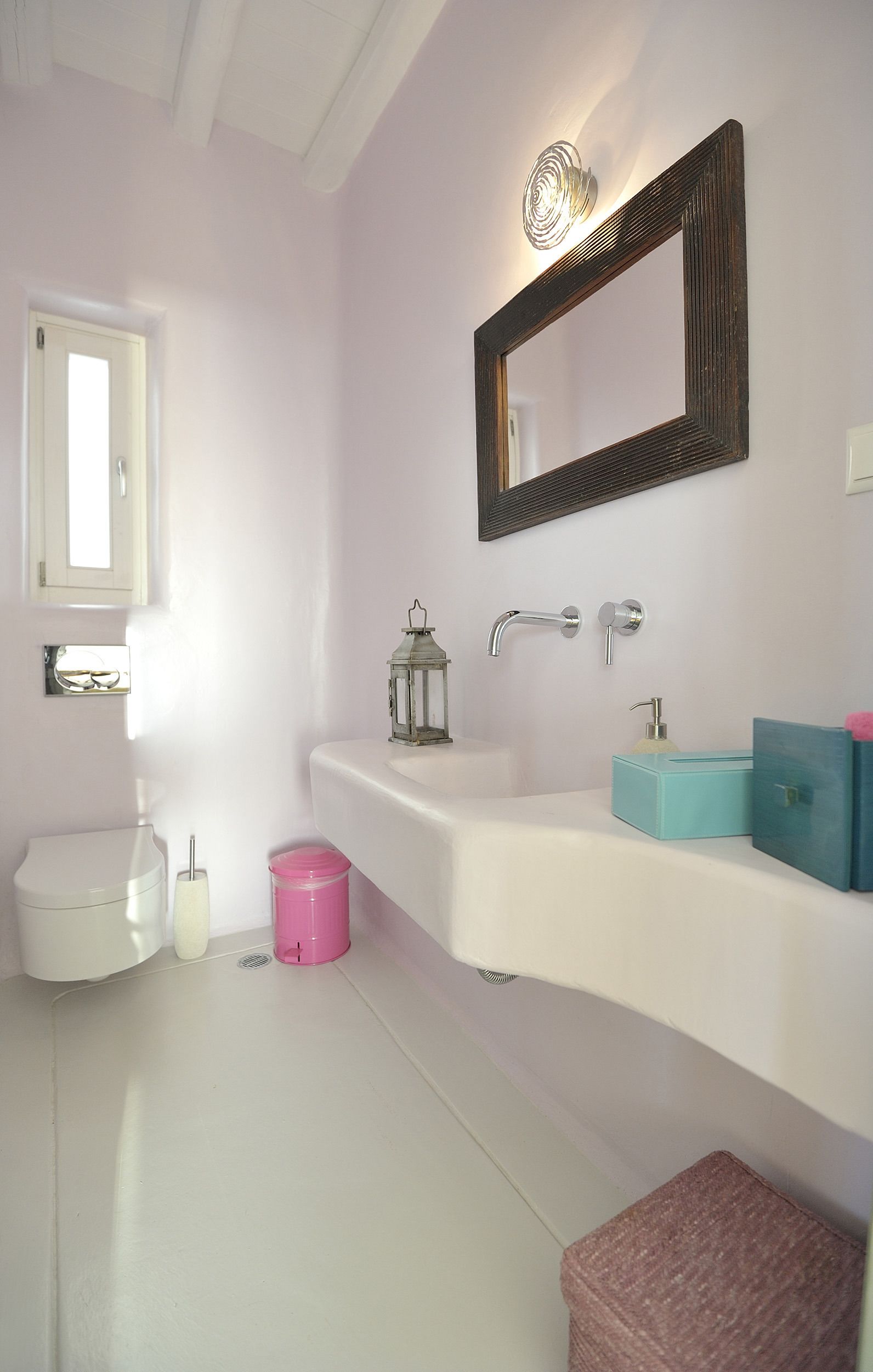 Een badkamer met een wit wastafel, een spiegel, een toilet en een roze emmer.