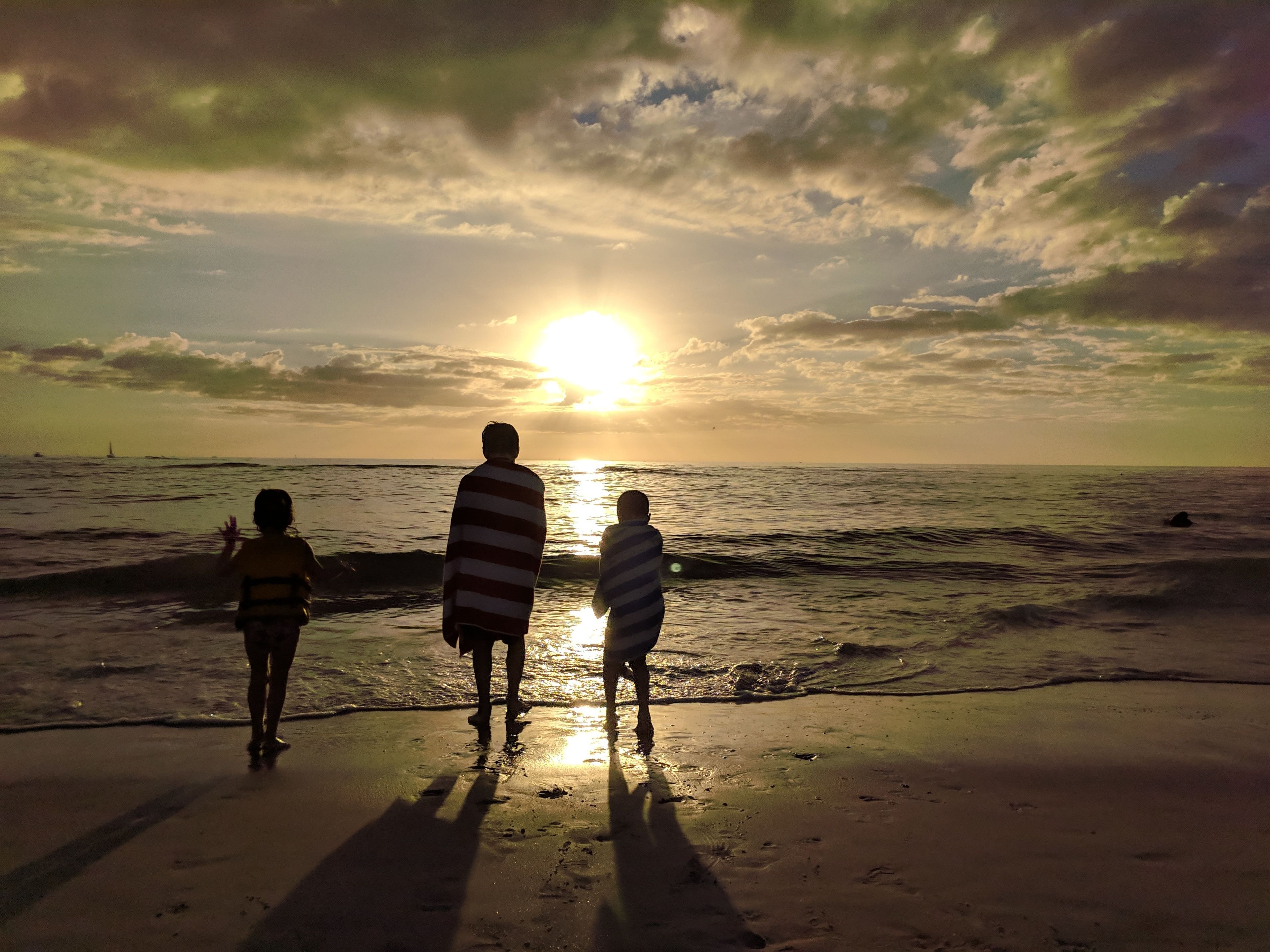 A sunset over the ocean with silhouettes of three people standing on the beach.