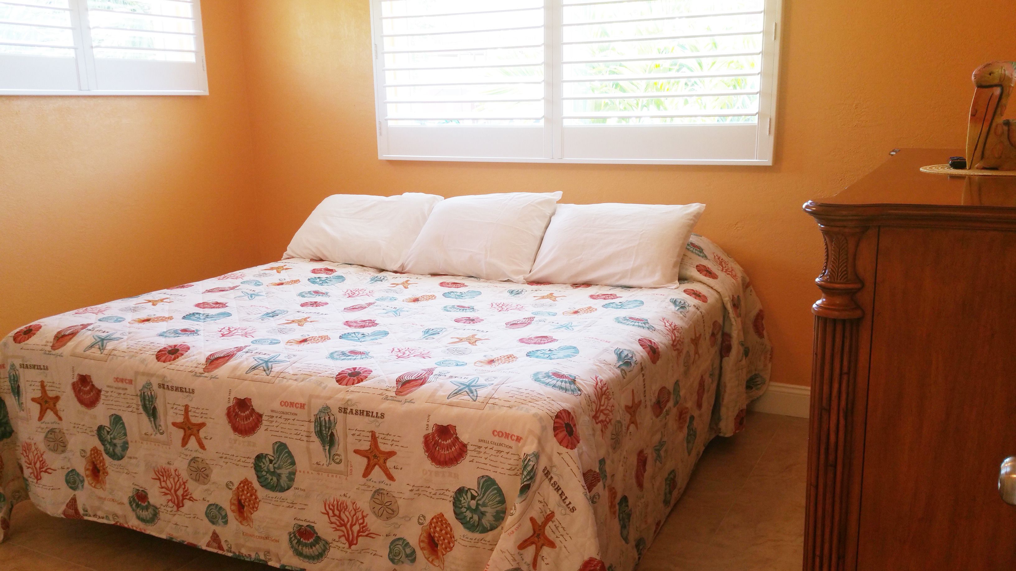 A bedroom with a bed, two windows, and a wooden dresser.