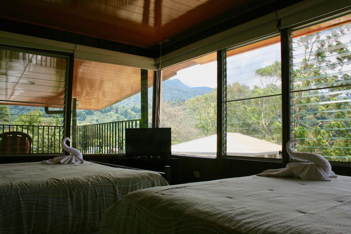 A room with two beds, a television, and large windows offering a view of a mountainous landscape.
