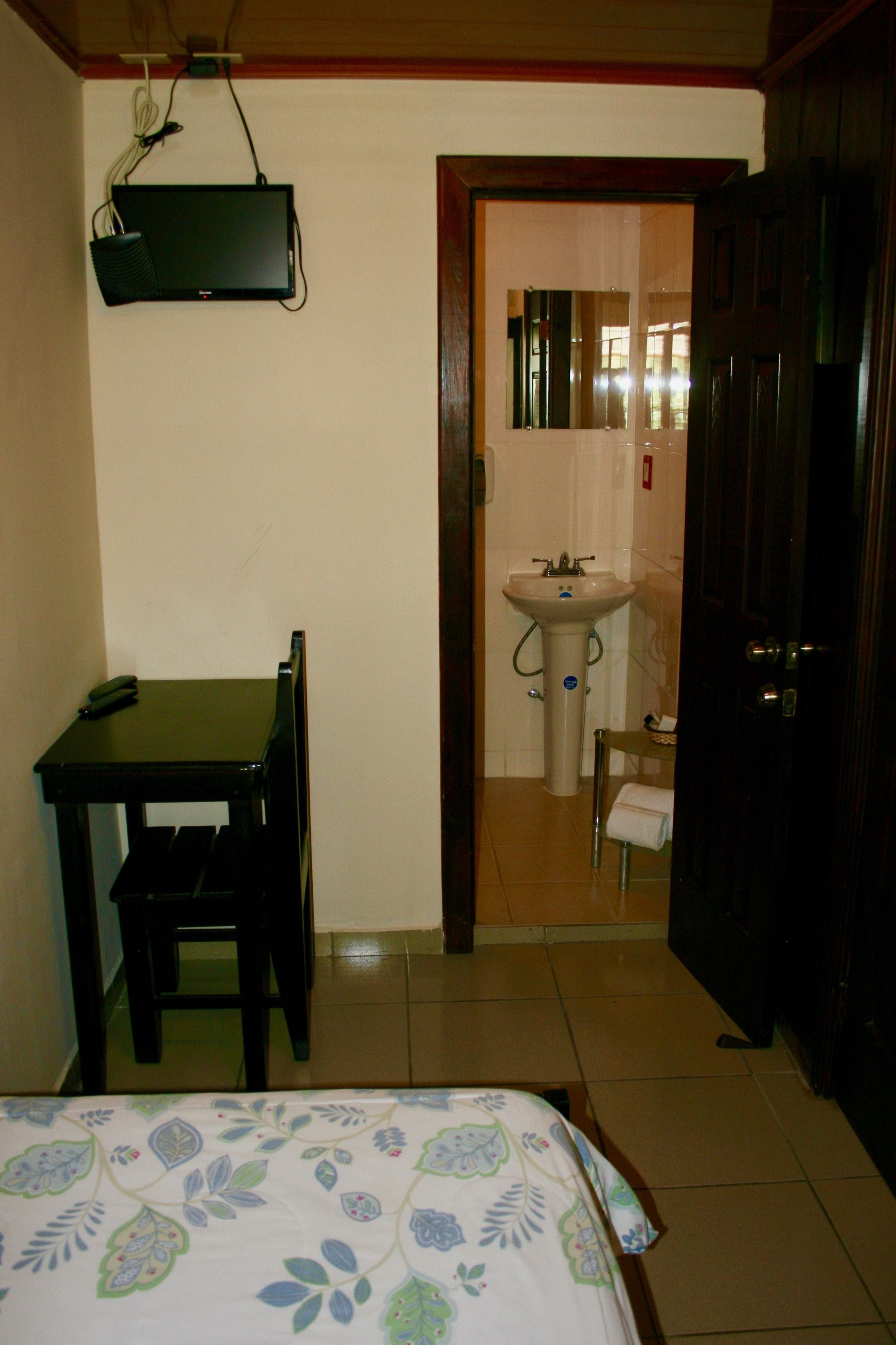 A small room with a bed, a desk, a chair, a sink, and a wardrobe.