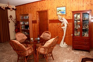 A dining area with a round table surrounded by wicker chairs, a wooden cabinet with glass doors, and a bookshelf against the wall. - Hotel Dimitra Sun (Rhodes)