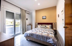 A bedroom with a large bed, a sliding glass door to a balcony, a small desk, and a nightstand. - Hotel Dimitra Sun (Rhodes)