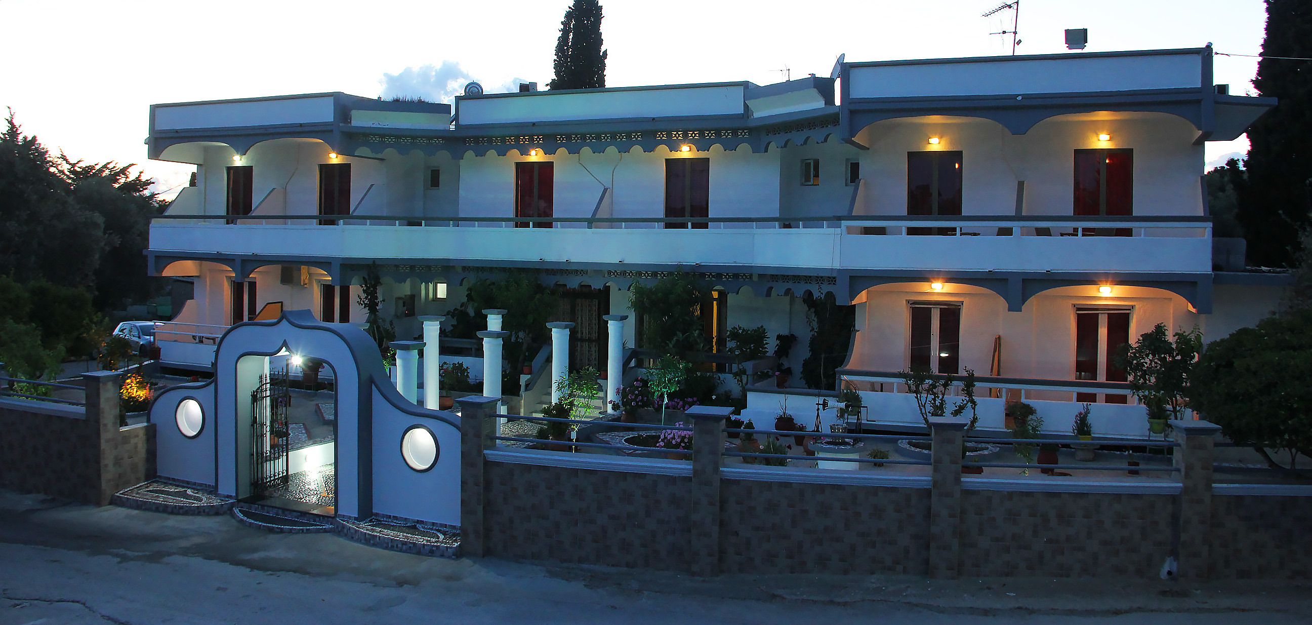 A two-story building with a balcony, a gated entrance, and potted plants.