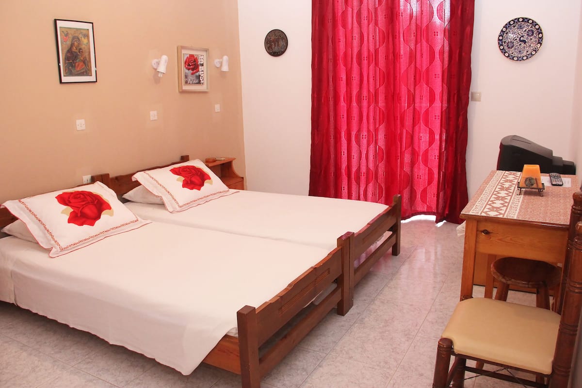 A room with two wooden beds, a desk with a chair, and a red curtain.