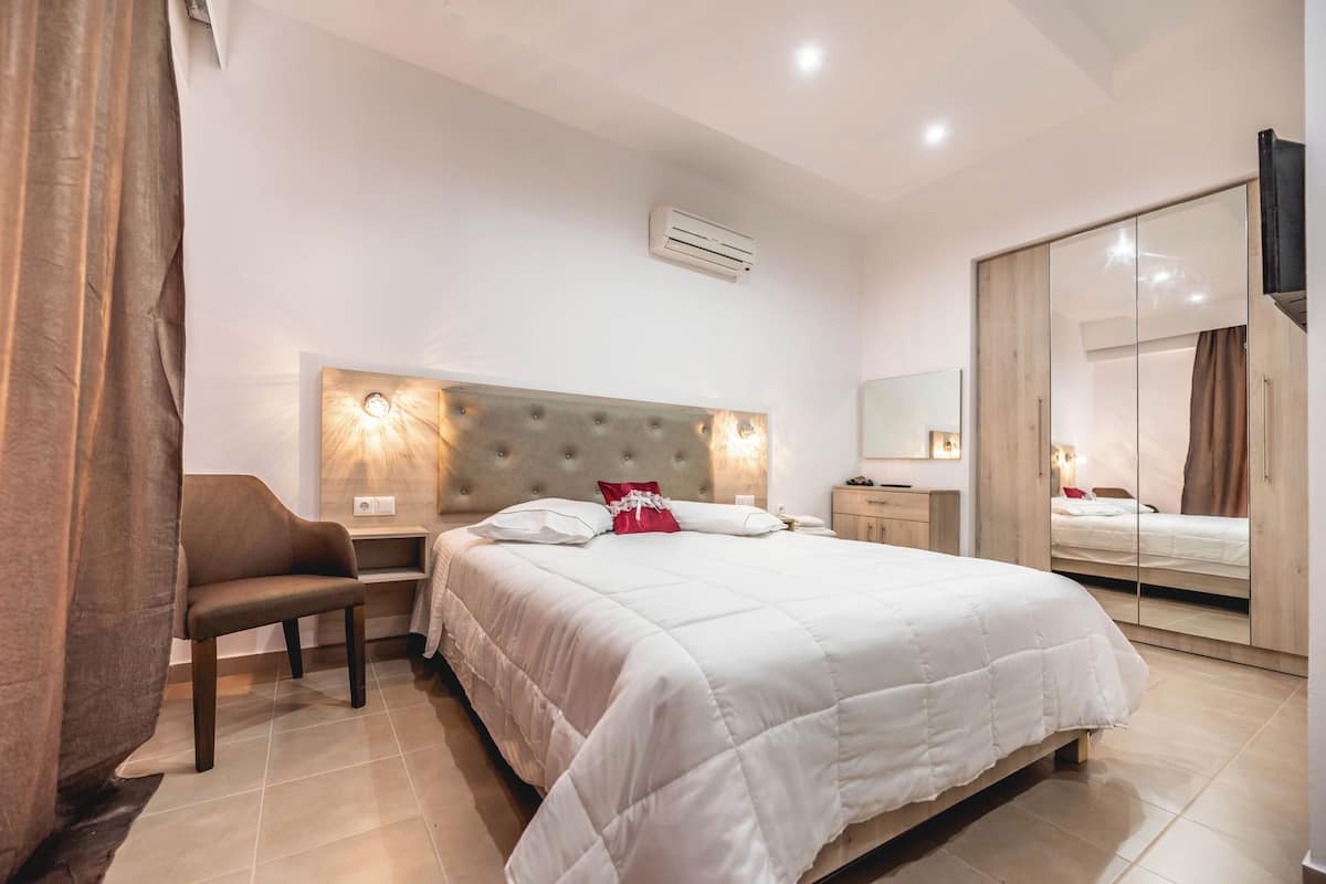 A hotel room with a bed, a chair, a bedside table, a mirror, and a wardrobe.