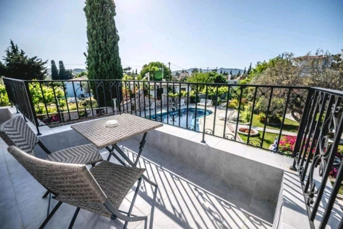 A balcony with a pool, wicker furniture, and a view of a garden and buildings.