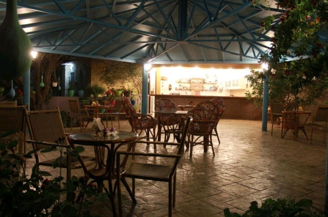 An outdoor patio with wicker furniture and a tiled floor, under a blue metal roof structure.