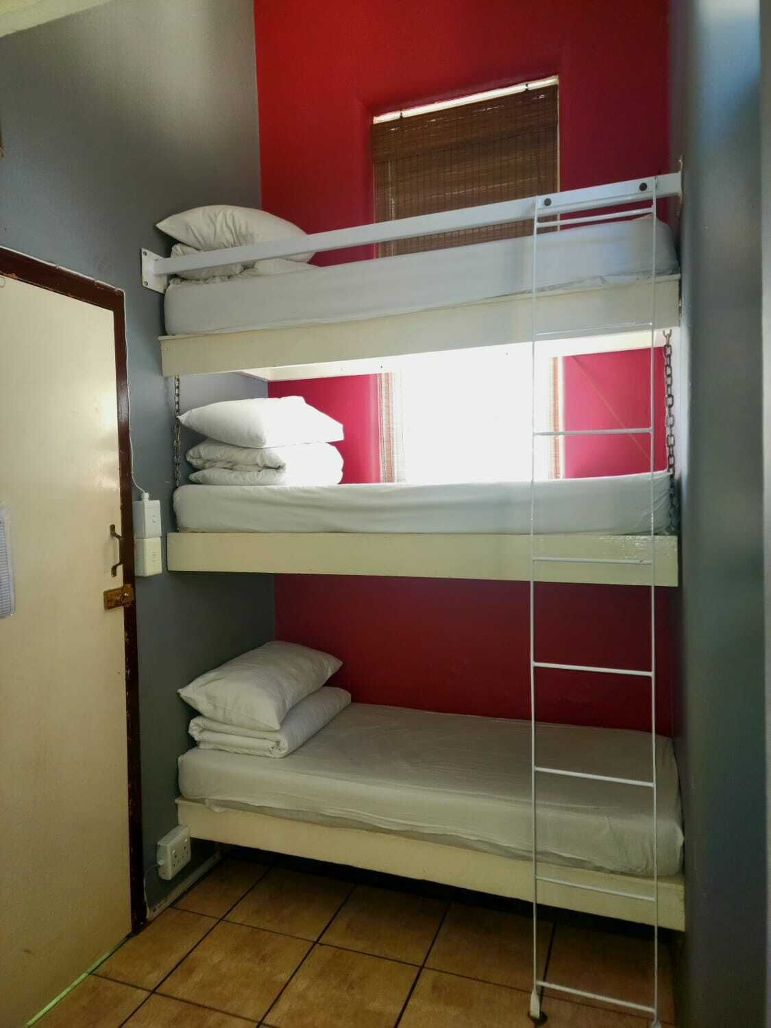 A bunk bed room with a red wall and a window.