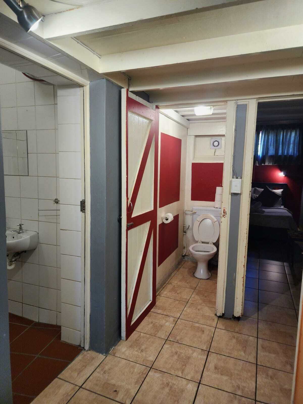 En smal hall med en röd dörr, ett vitt handfat och en toalett.