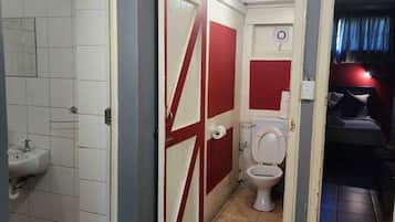 En smal hall med en röd dörr, ett vitt handfat och en toalett.