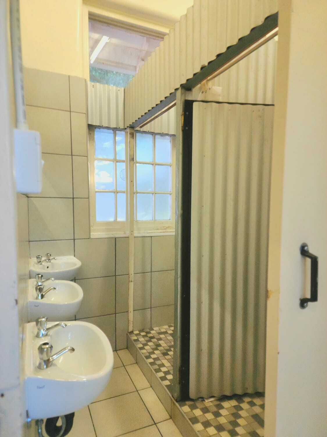 A bathroom with three sinks, a window, and a shower area.