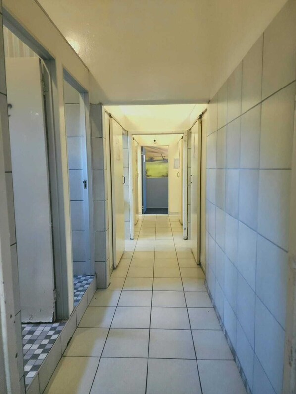 Un couloir au sol carrelé, avec des portes de chaque côté, qui mène à une pièce offrant une vue sur un paysage verdoyant.