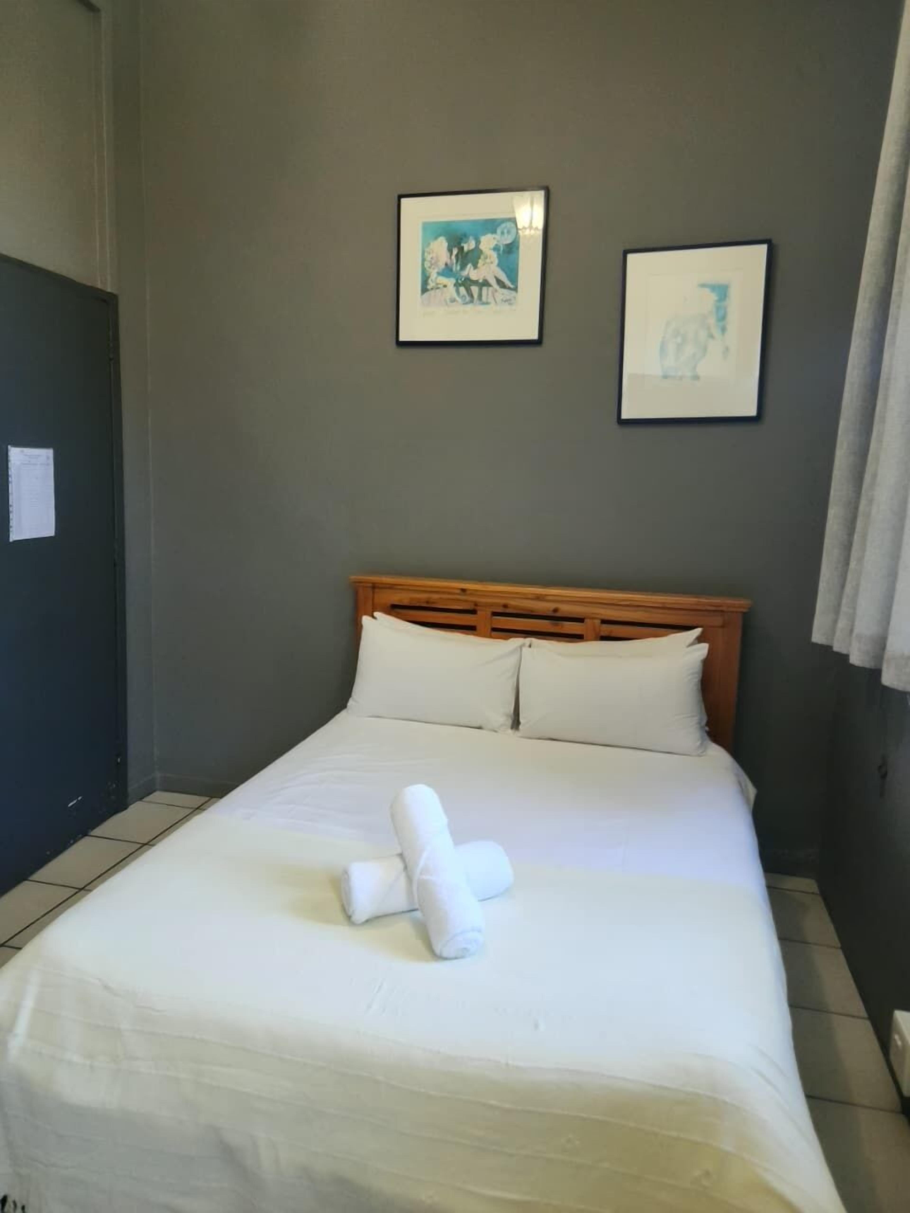 A neatly made bed with white linens and towels, a wooden headboard, and two framed pictures on the wall.