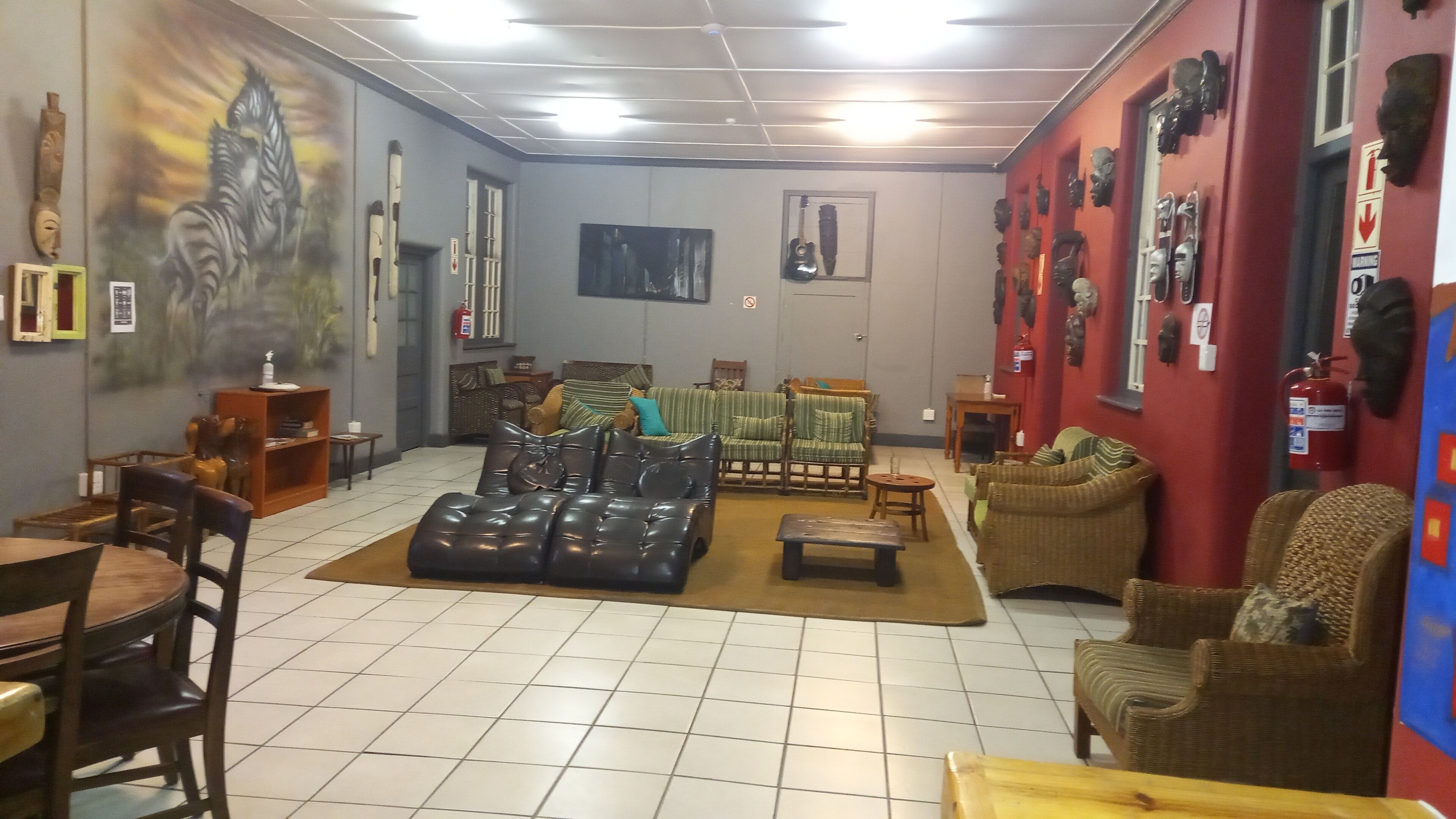 Een kamer met een groot schilderij van een zebra, een gitaar en diverse maskers aan de muren. Er zijn meerdere zithoeken met banken en stoelen.