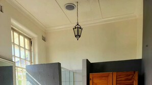 Camera da letto con un letto, un armadio in legno, bagno con specchio, lavabo e doccia, e una lampada a sospensione.