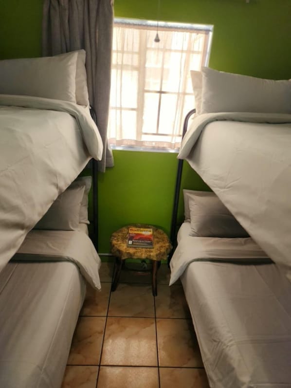A room with two bunk beds, a small stool with a book, and a window with curtains. - Riverlodge Backpackers (Cape Town)