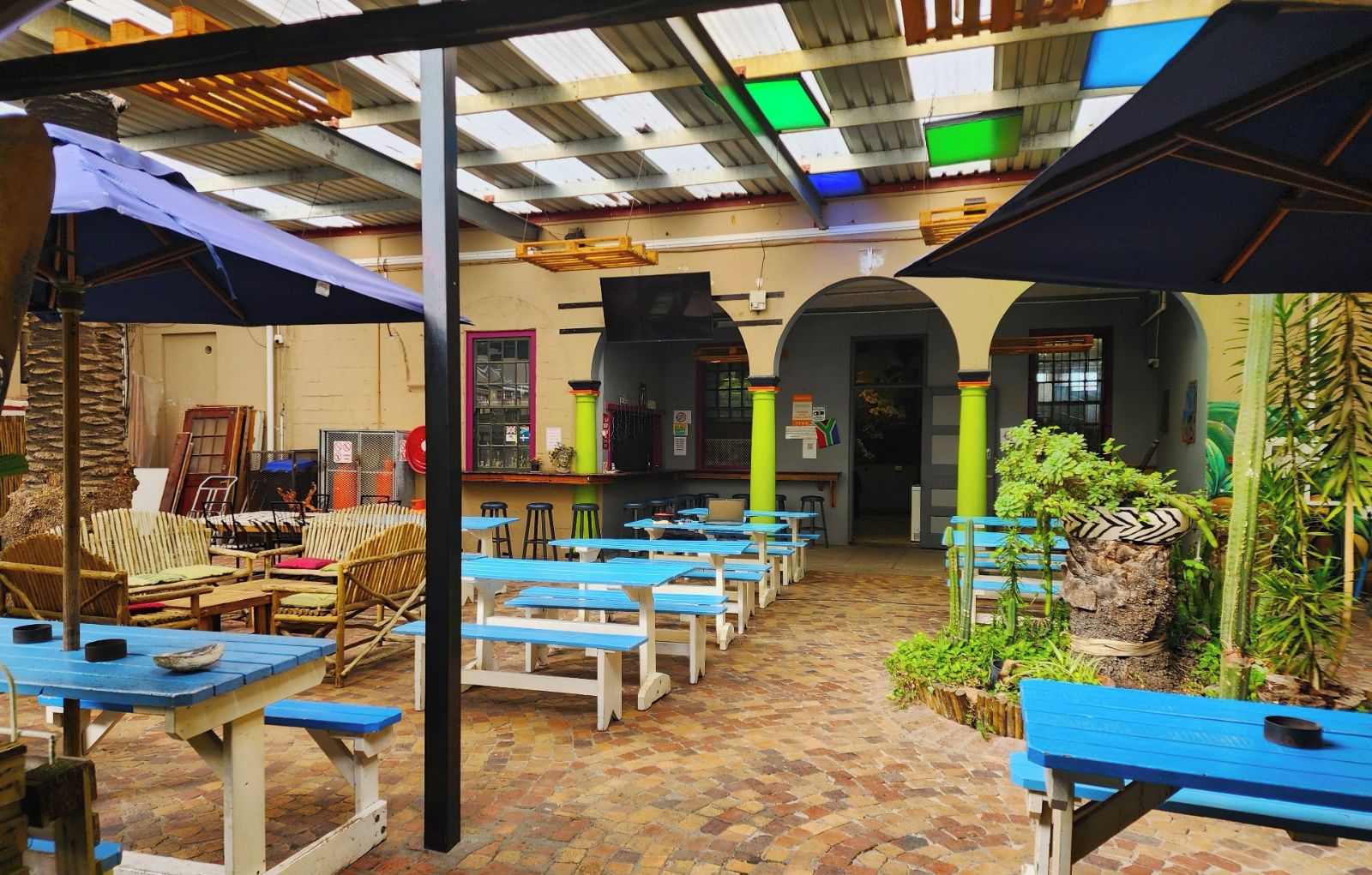 A restaurant with outdoor seating, brick flooring, and a mix of wooden and metal furniture.