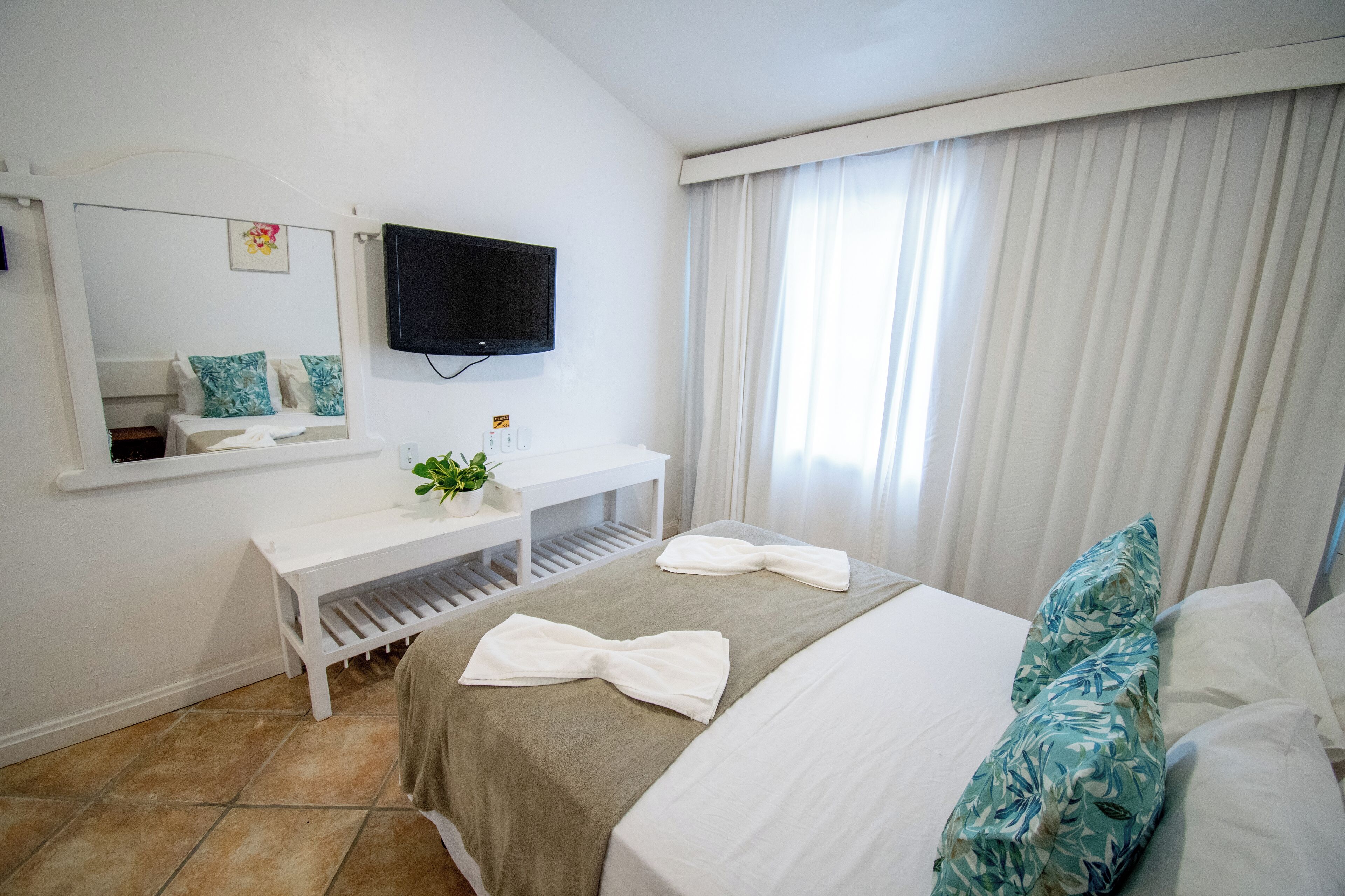 Une chambre d’hôtel avec un lit, un bureau, une télévision et une fenêtre avec des rideaux.