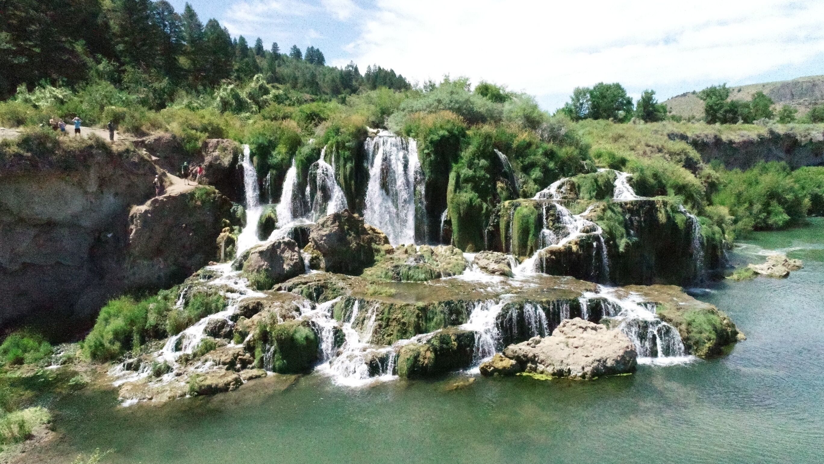 Une cascade naturelle comportant plusieurs chutes d’eau, le tout entouré d’une végétation luxuriante et d’arbres.