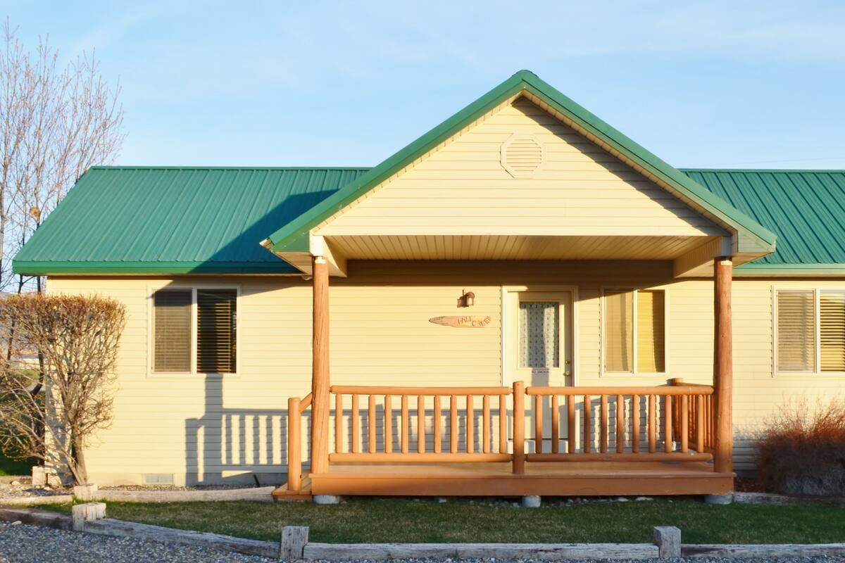 A single-story building with a green roof and a porch with a wooden railing.