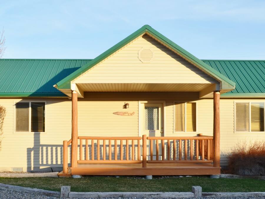 A single-story building with a green roof and a porch with a wooden railing.