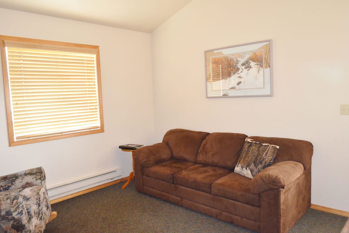 A living room with a brown sofa, a framed picture on the wall, and a window with blinds.