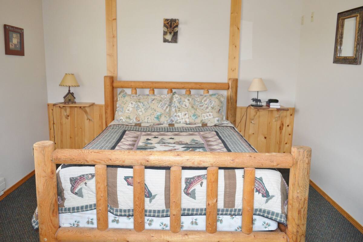A wooden bed with a quilt and pillows, two bedside tables with lamps, and a framed picture on the wall.