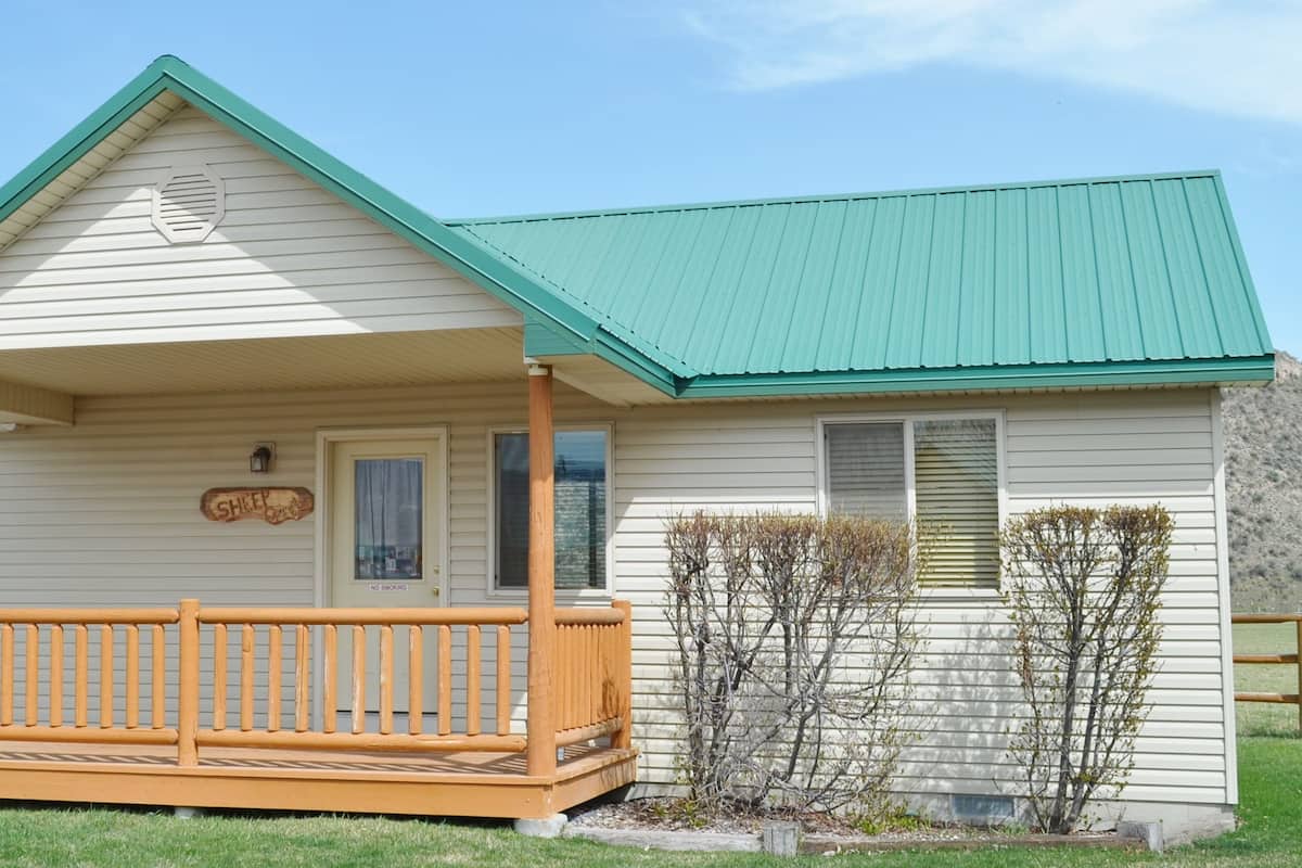A single-story house with a green roof, a porch with a wooden railing, and a 'No Smoking' sign.