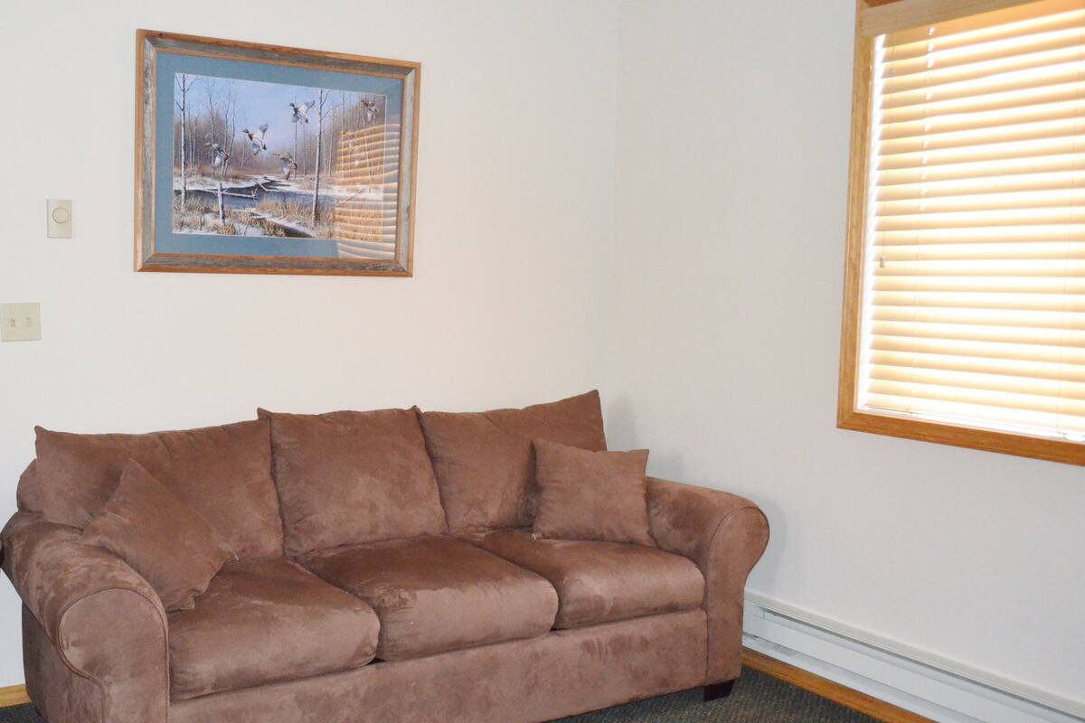 A brown sofa in a room with a framed painting on the wall and a window with blinds.