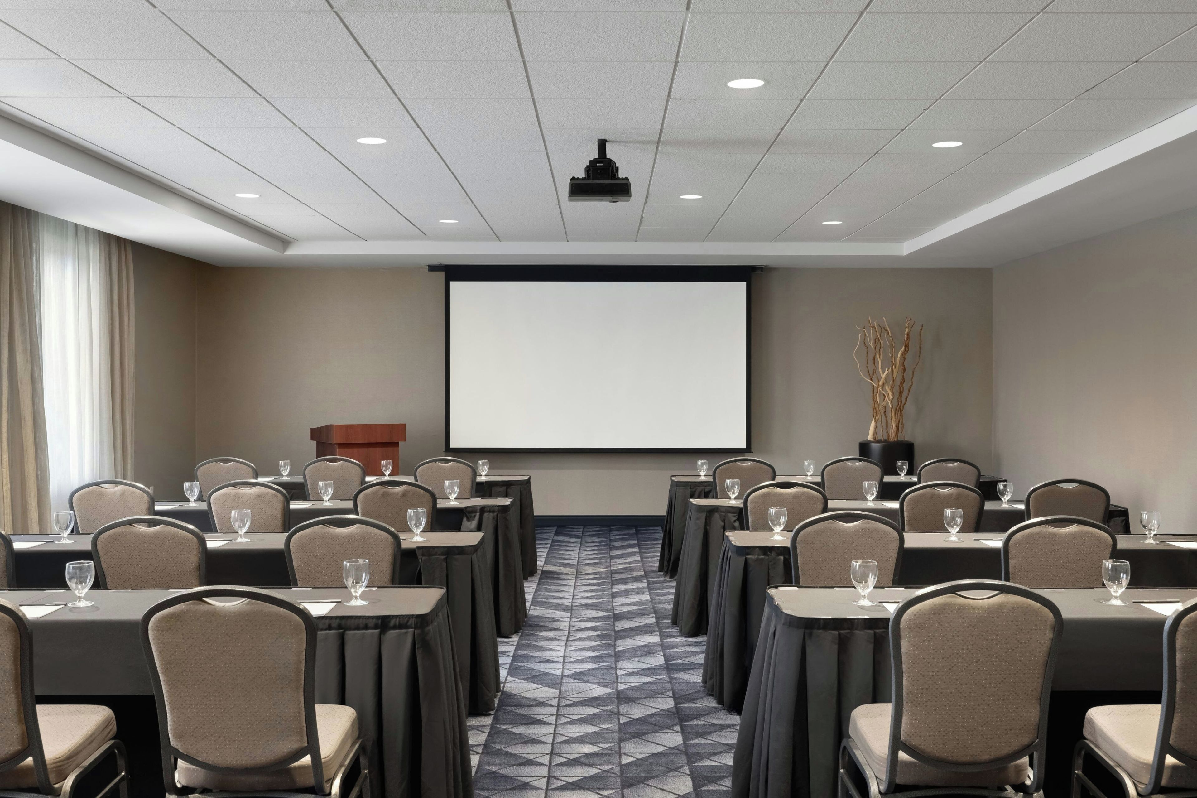 A conference room with a large screen, multiple tables, and chairs arranged for a meeting.