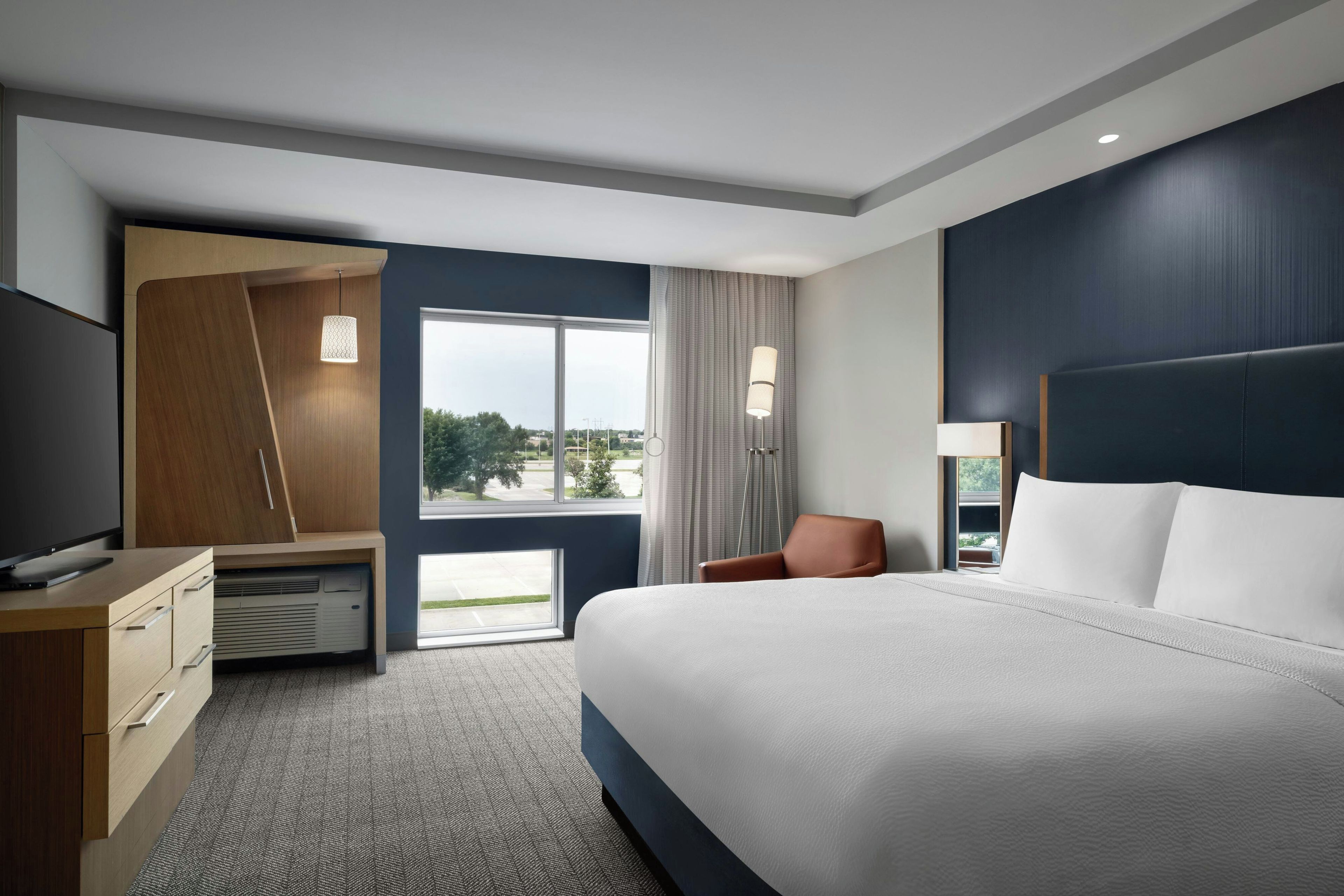 Habitación de hotel con una cama grande, un escritorio, un televisor de pantalla plana, una silla y vistas al exterior.