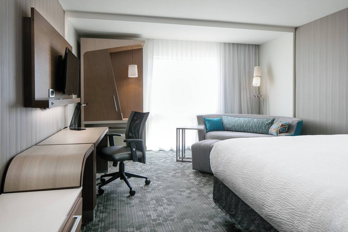 A hotel room with a bed, a desk, a chair, a TV, and a lamp.