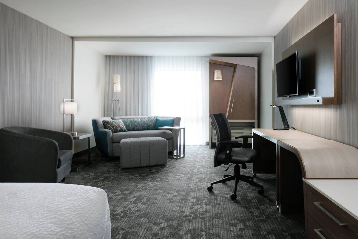 A hotel room with a bed, a desk, a sofa, a TV, and a window with curtains.